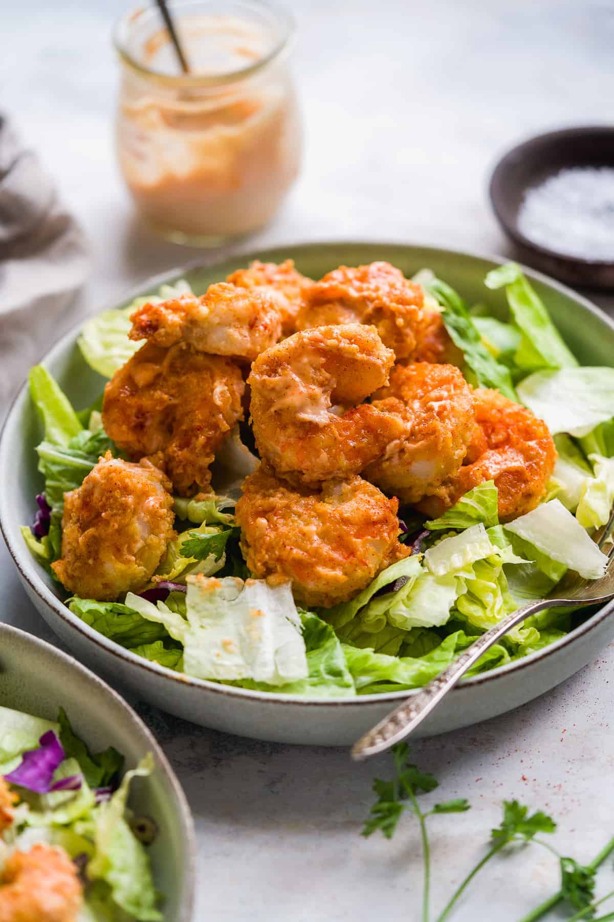 Orange shrimp tossed in sauce on a plate of lettuce.