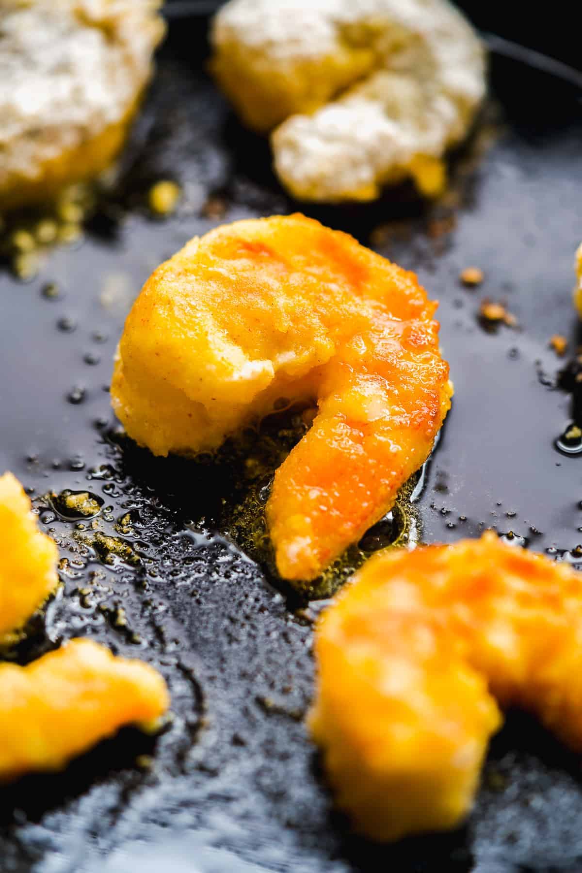 Black skillet with breaded shrimp cooking in oil.