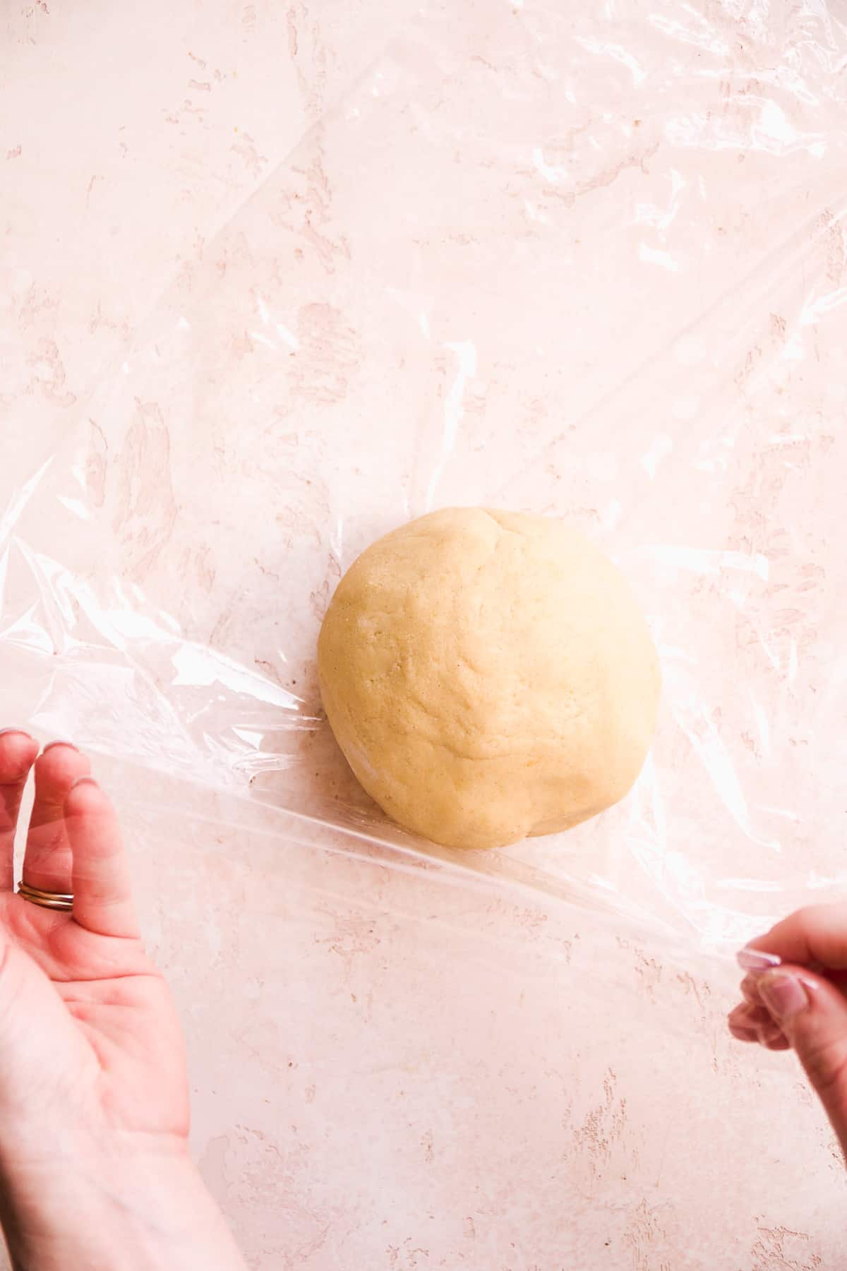 Hand wrapping a ball of dough in plastic wrap.