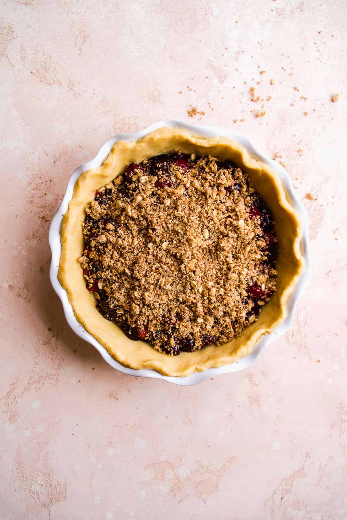 Unbaked gluten free cherry pie with crumble on a pink surface.