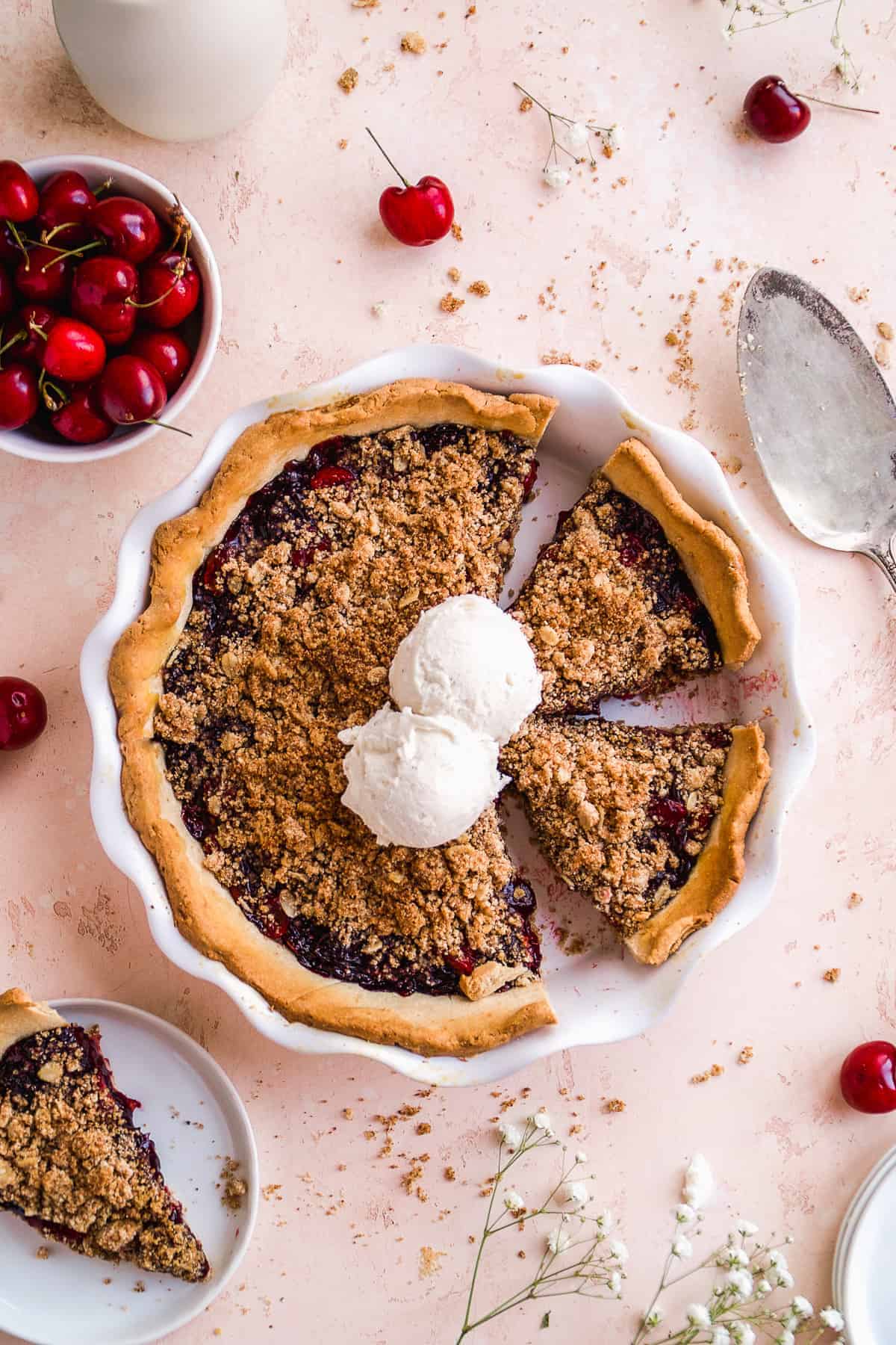 Gluten free cherry crumble pie in a white pie pan with ice cream scoops on top.