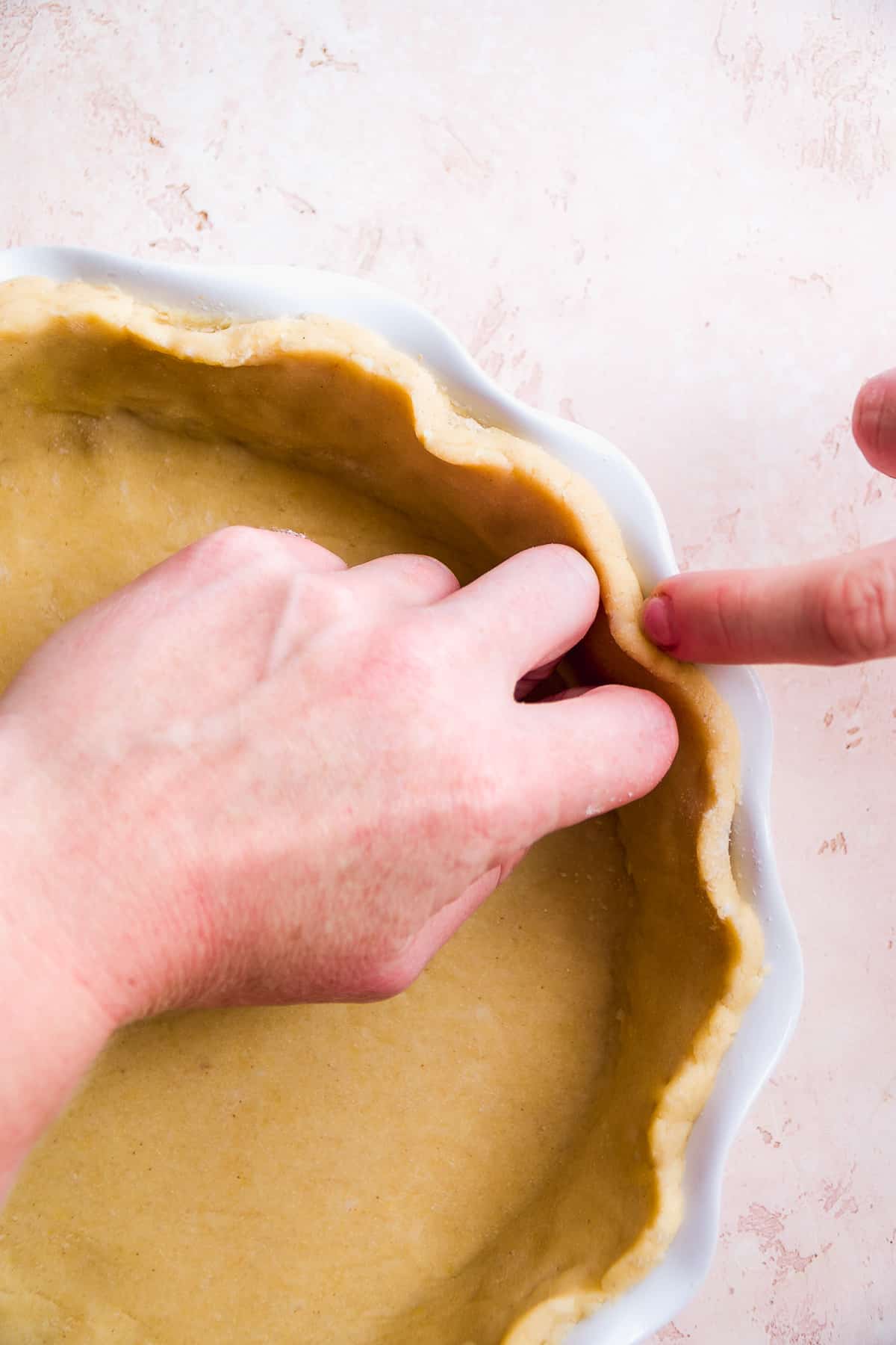 Hand pressing the edges of a pie crust to make a ruffle edge.