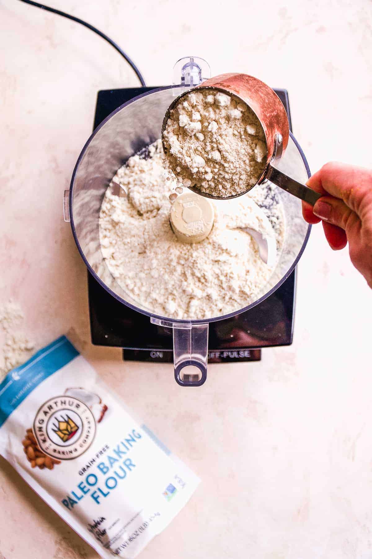 Hand pouring flour into a food processor. 