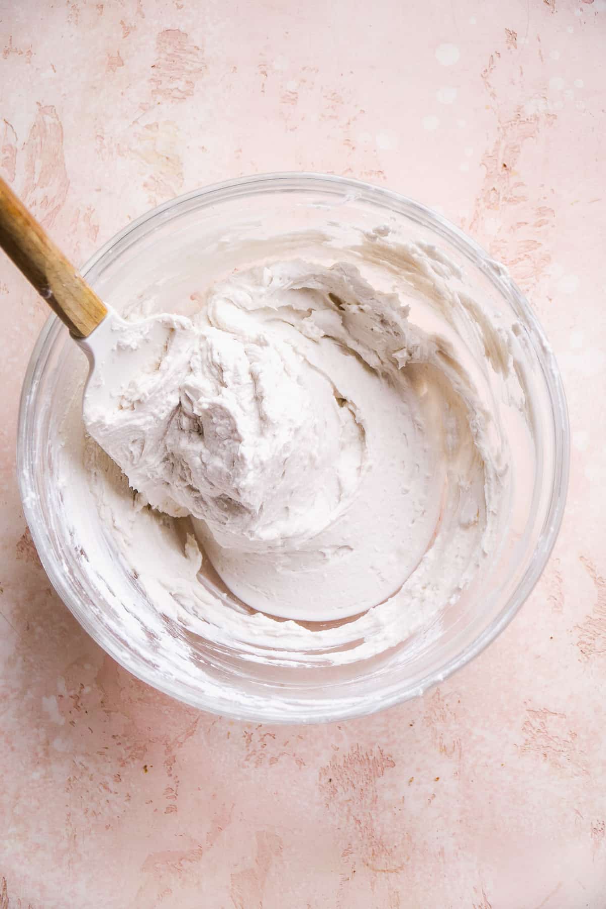Coconut whipped cream in a glass mixing bowl with a spatula.