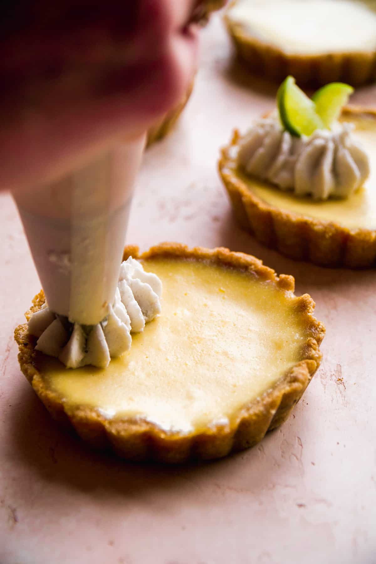 Hand pipping whipped cream onto a gluten free key lime pie.