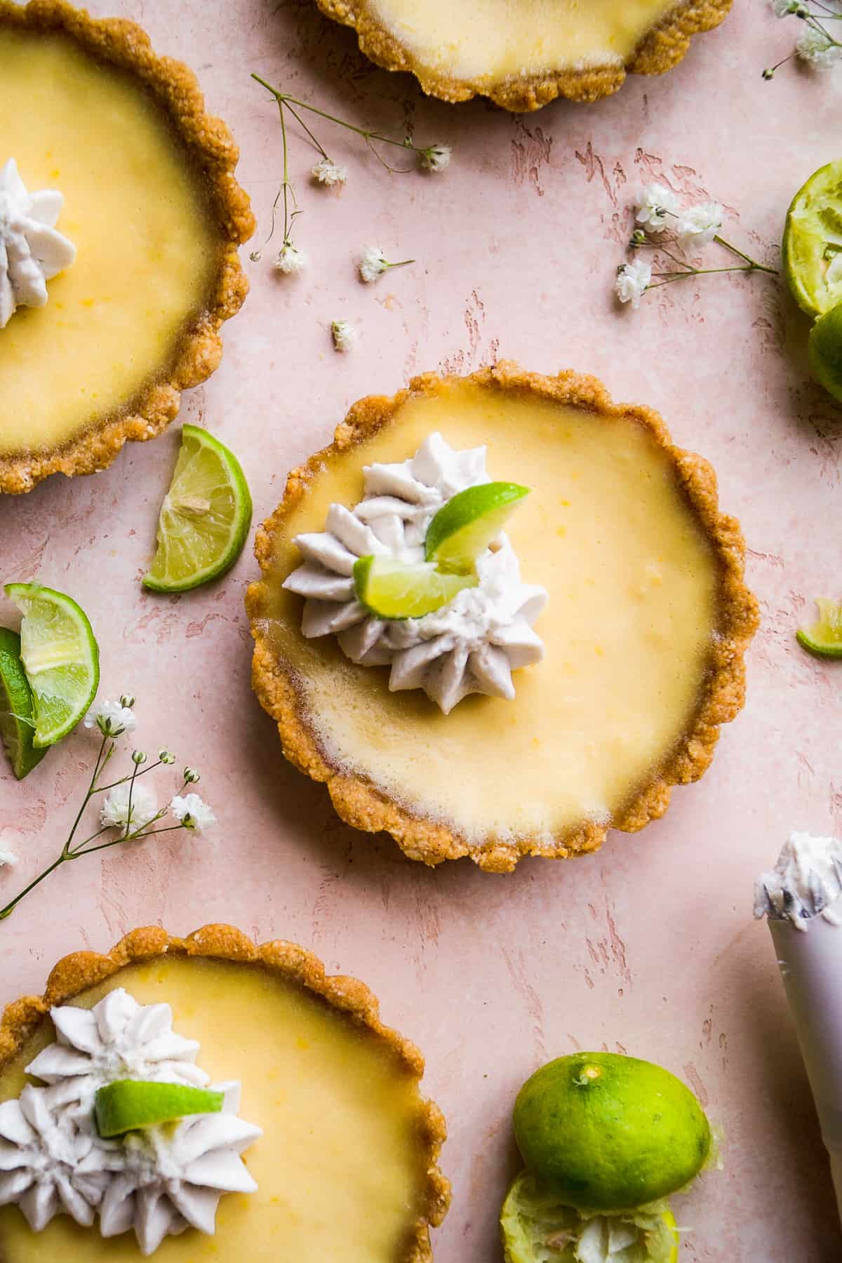Key lime pie tarts on a pink surface with whipped cream on top.