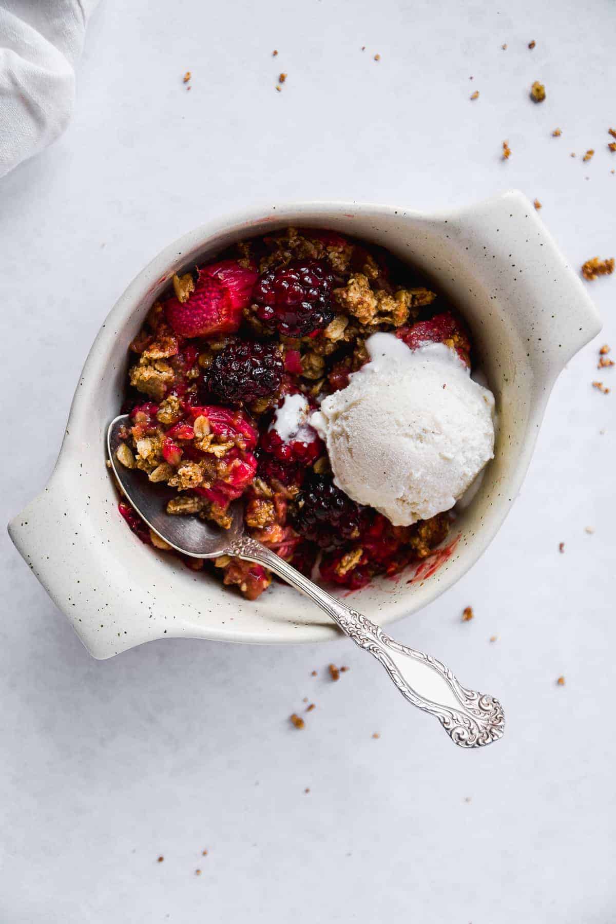 Bowl of gluten free rhubarb crisp with ice cream scoop on top and a spoon.