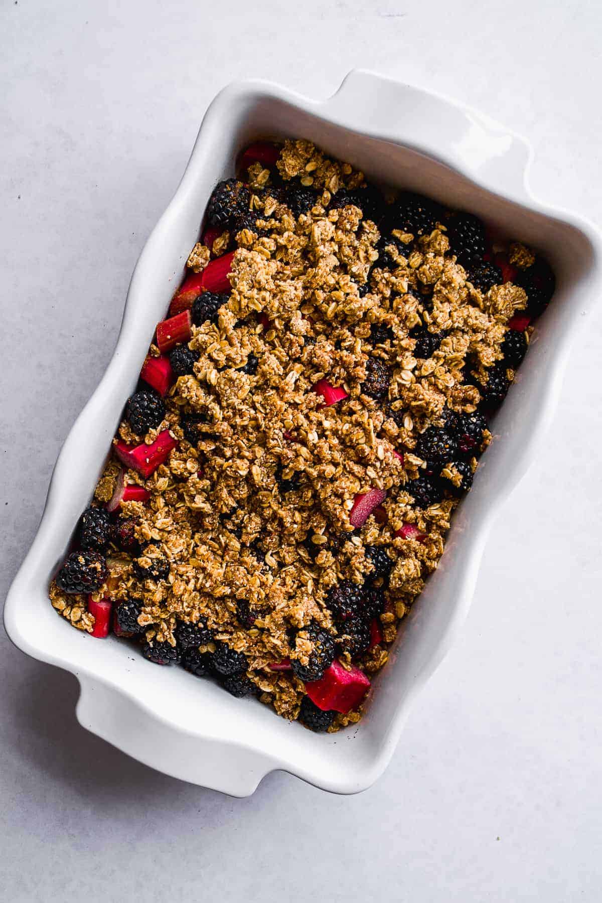 White dish with sliced rhubarb and blackberries and a gluten free crumble on top.