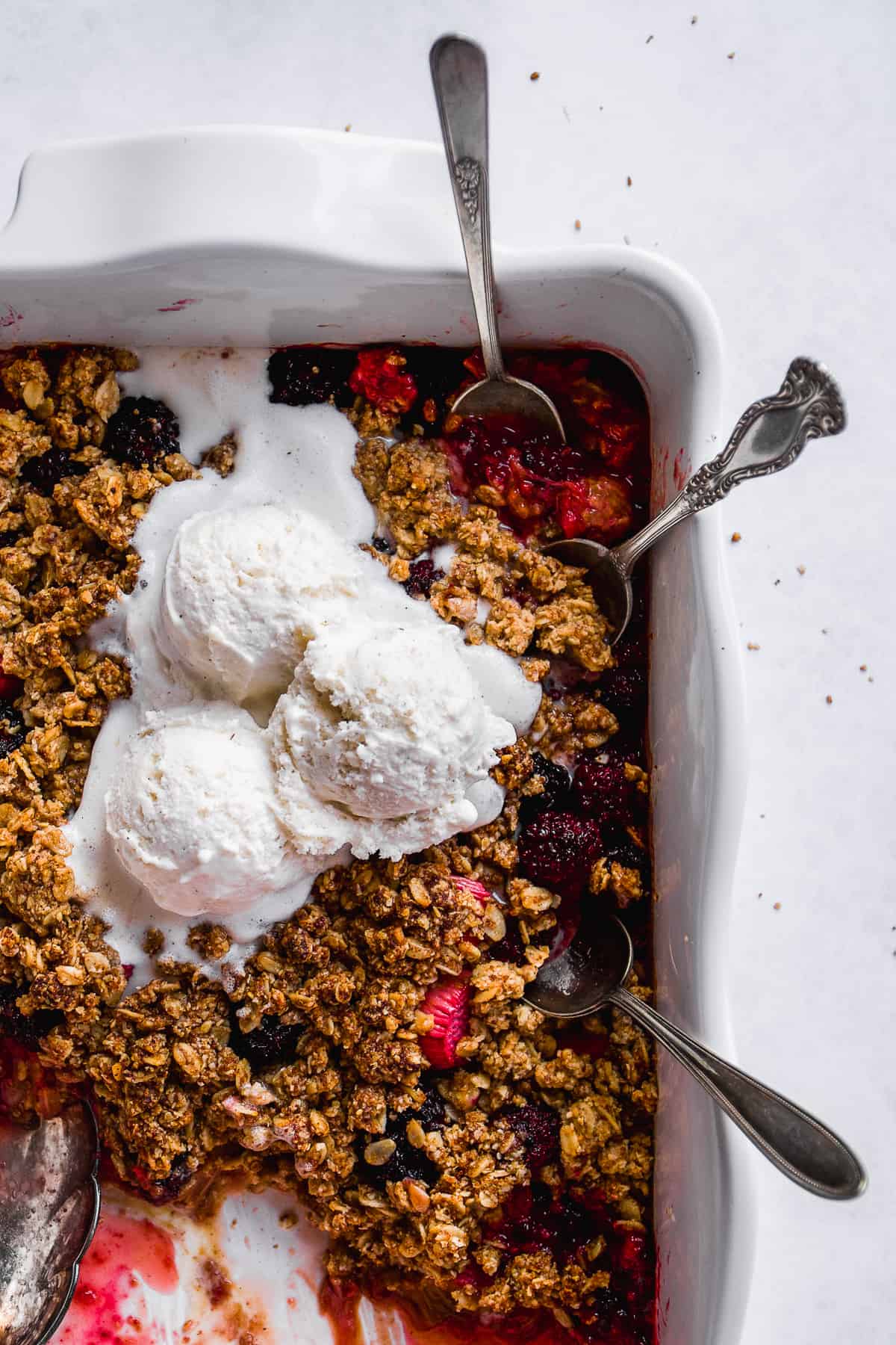 Gluten free rhubarb crisp in a white dish with ice cream and spoons.