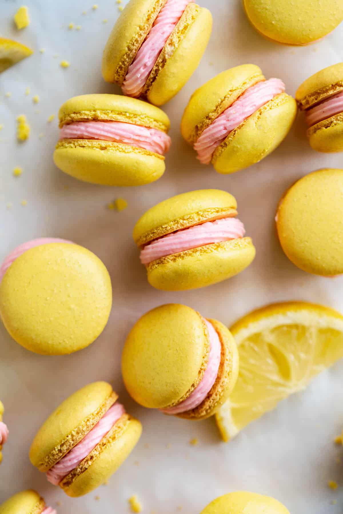 Pink lemonade macarons scattered on a white surface.