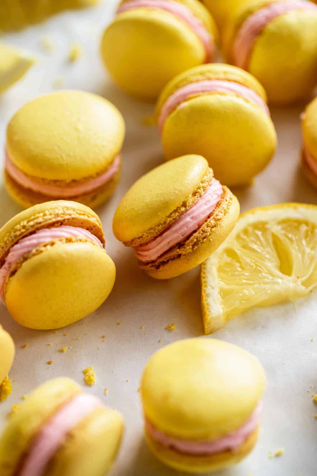 Lemonade macarons with pink icing scattered on surface with a lemon.