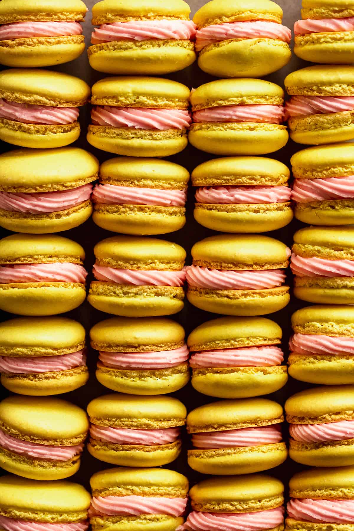 Lemonade macarons with pink icing lined up in rows.