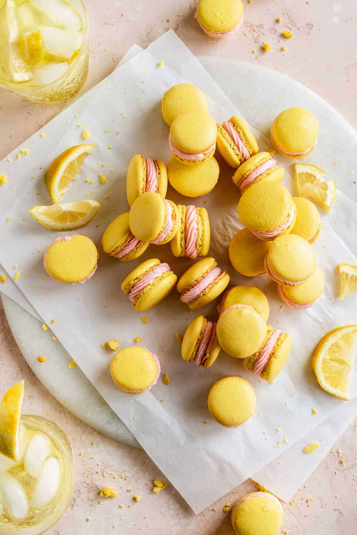 Lemon colored macarons with pink icing piled on round platter.