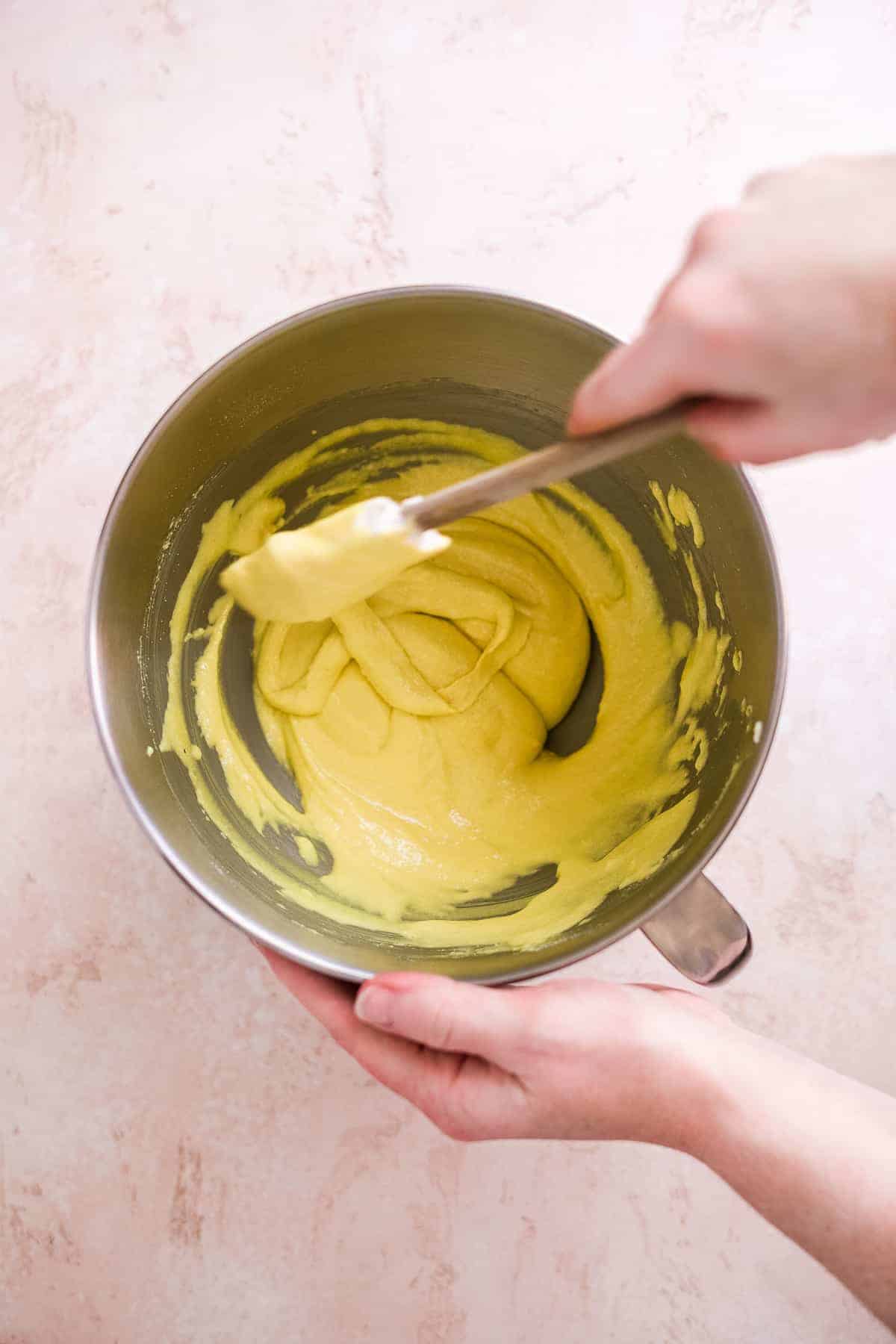 Person mixing lemonade macaron batter with a spatula.