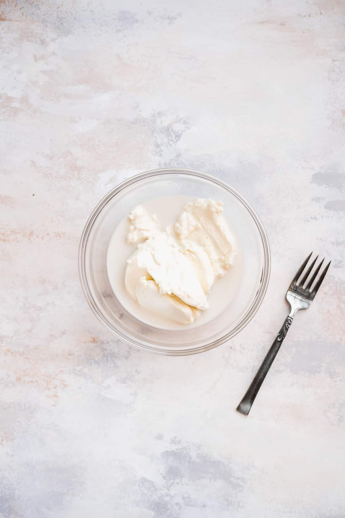 Glass bowl with ricotta cheese mixture and a fork on the side.