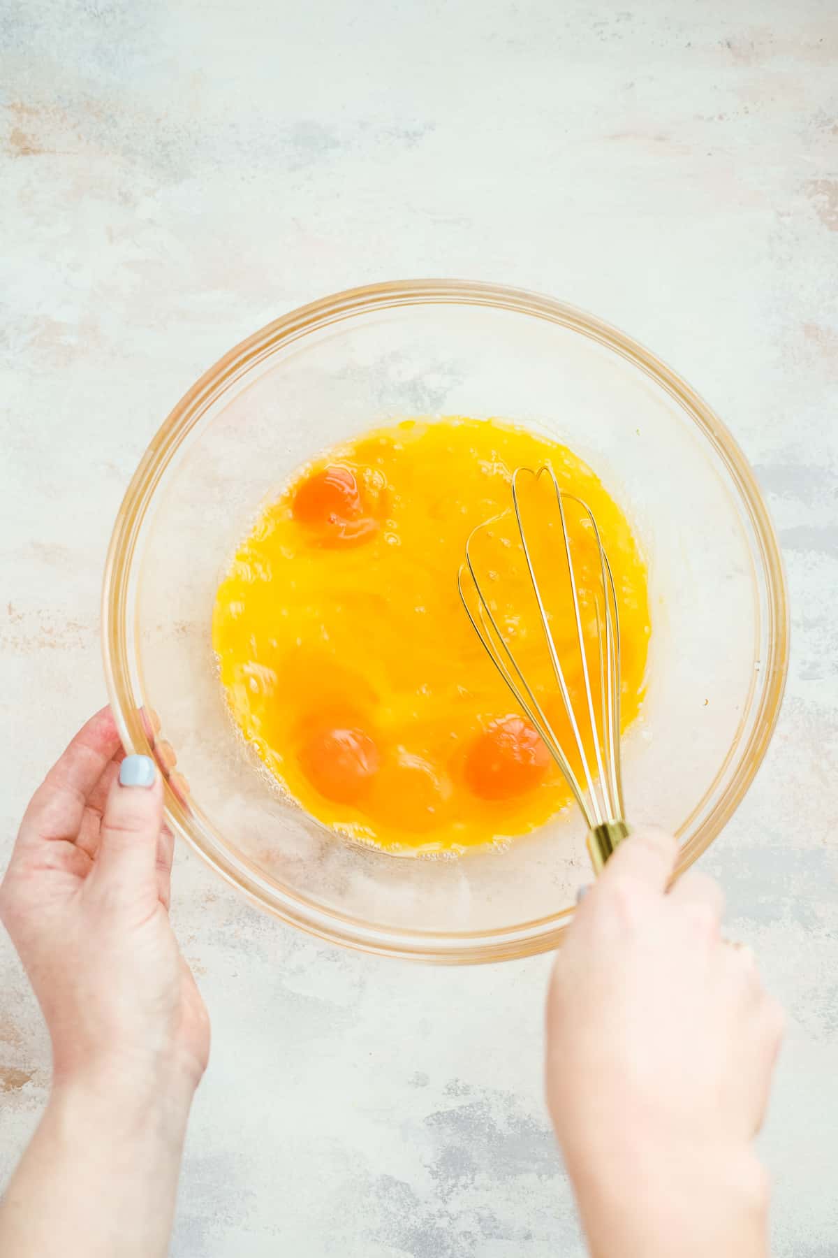 Hand whisking eggs in a glass mixing bowl.