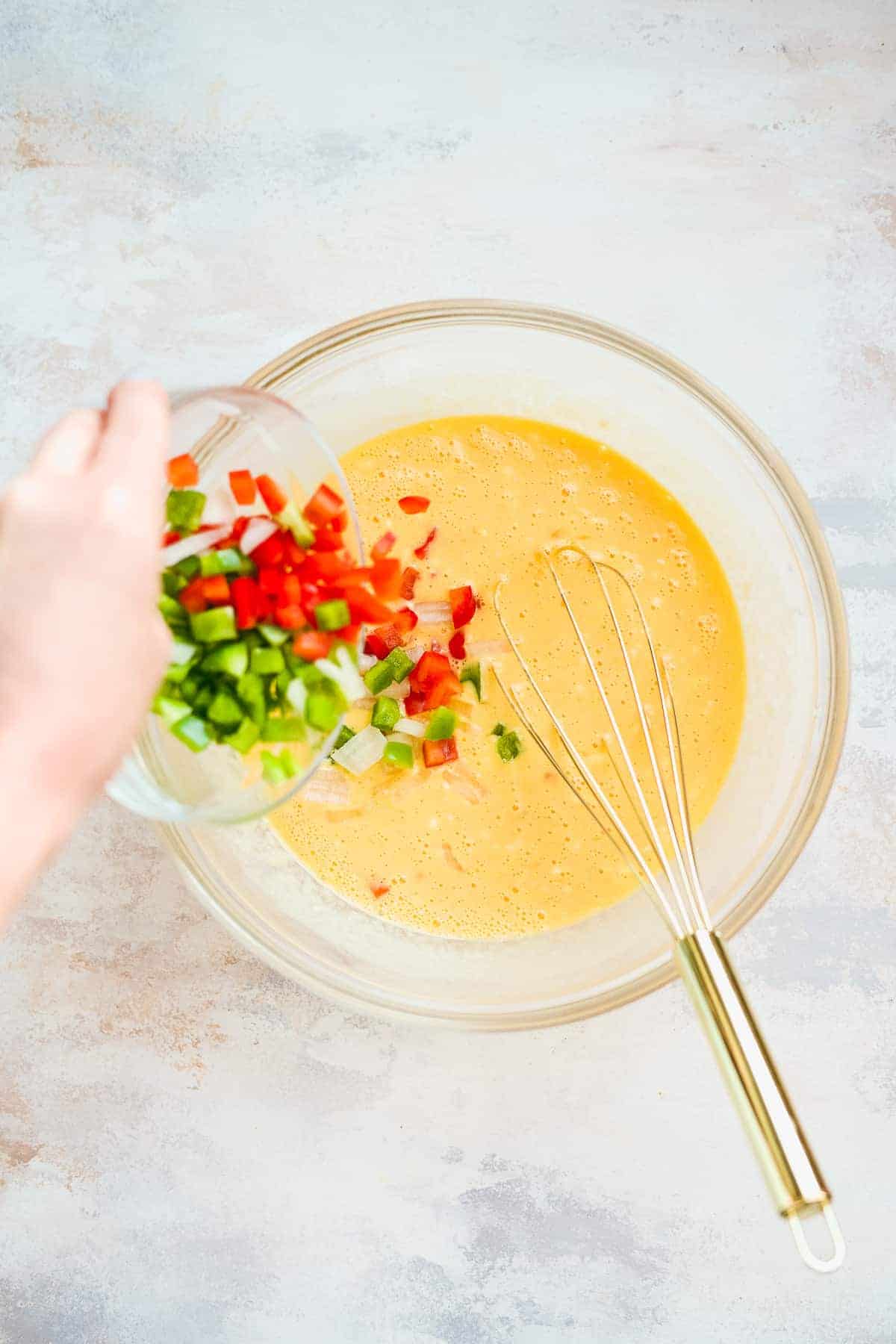 Person pouring peppers into a bowl with an egg mixture.