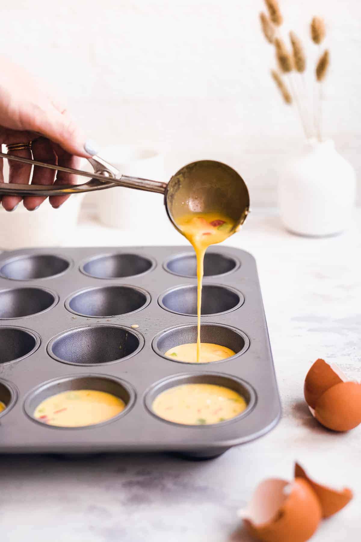 Hand pouring egg batter into a muffin tin.