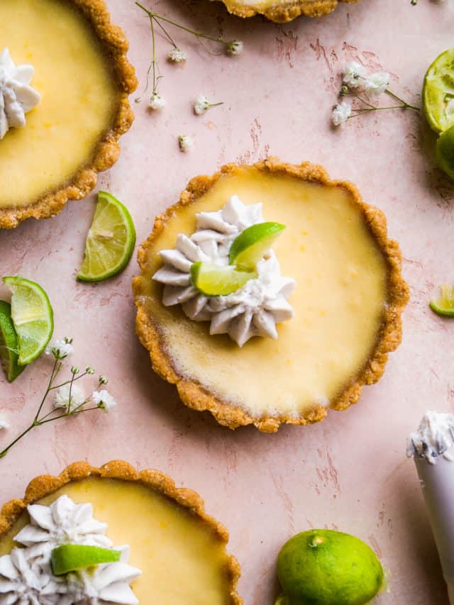Key lime pie tarts on a pink surface.