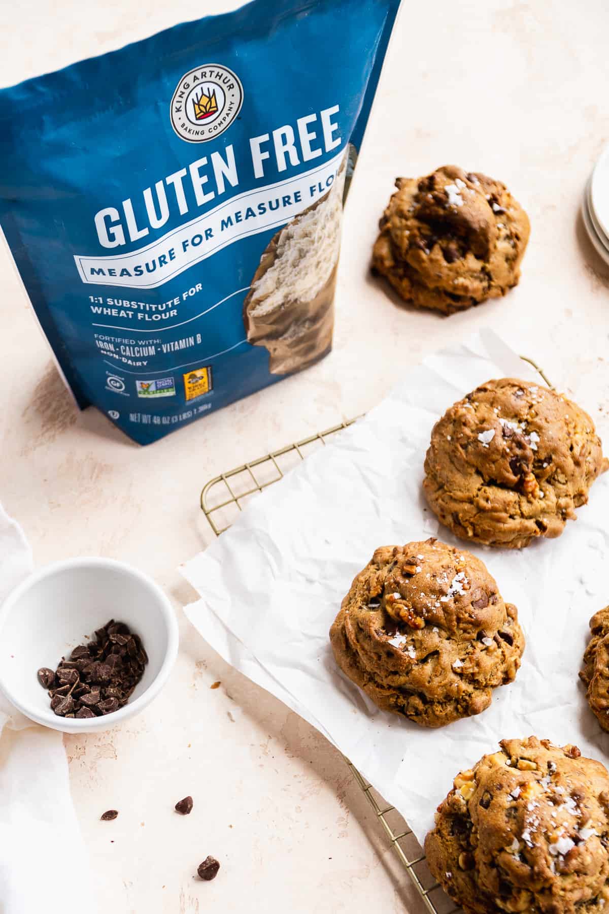 Chunky bakery style cookies on a cooling rack with a bag of gluten free flour next to the side.