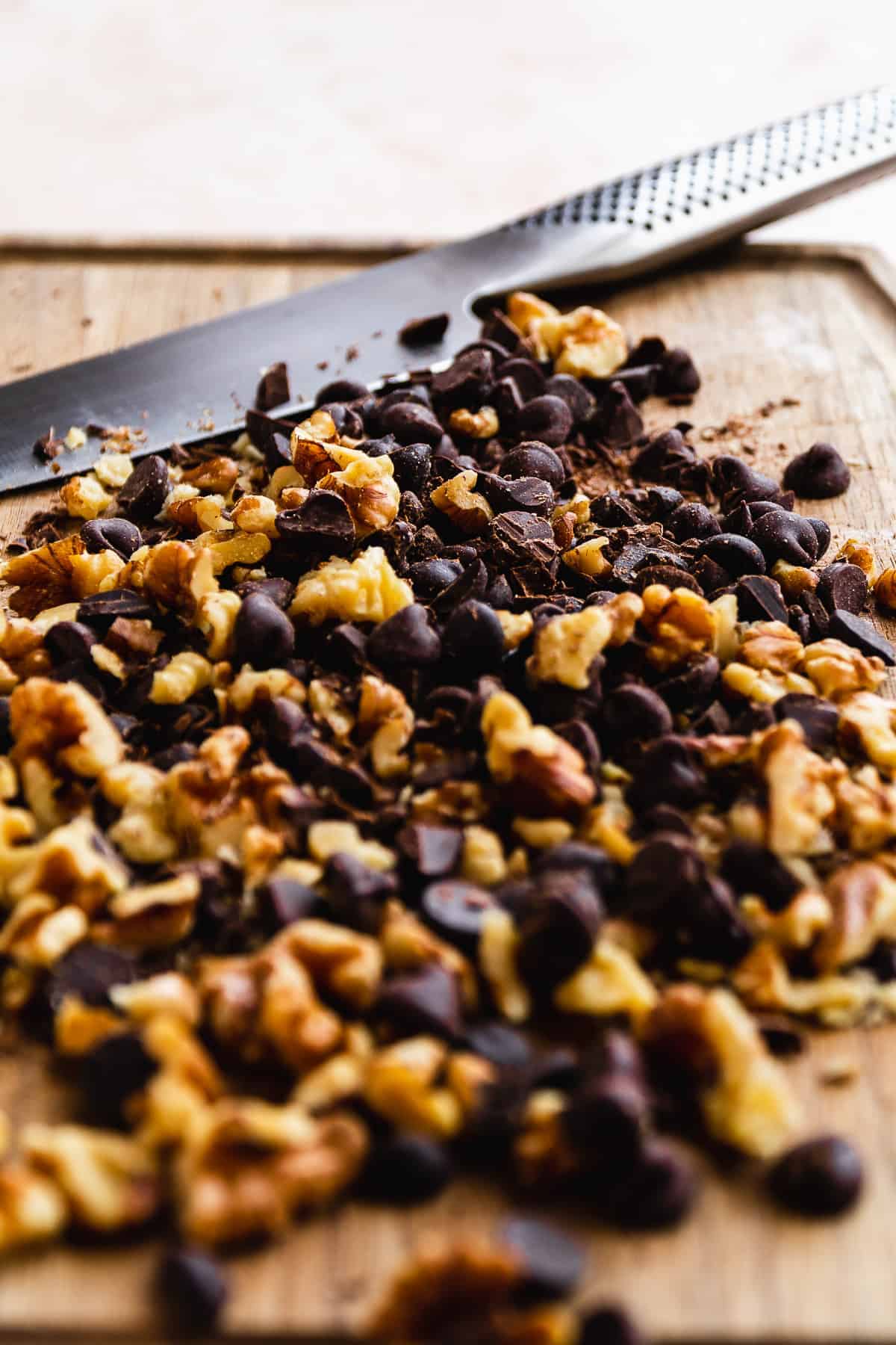 Chocolate and walnuts chopped on a cutting board with a knife.