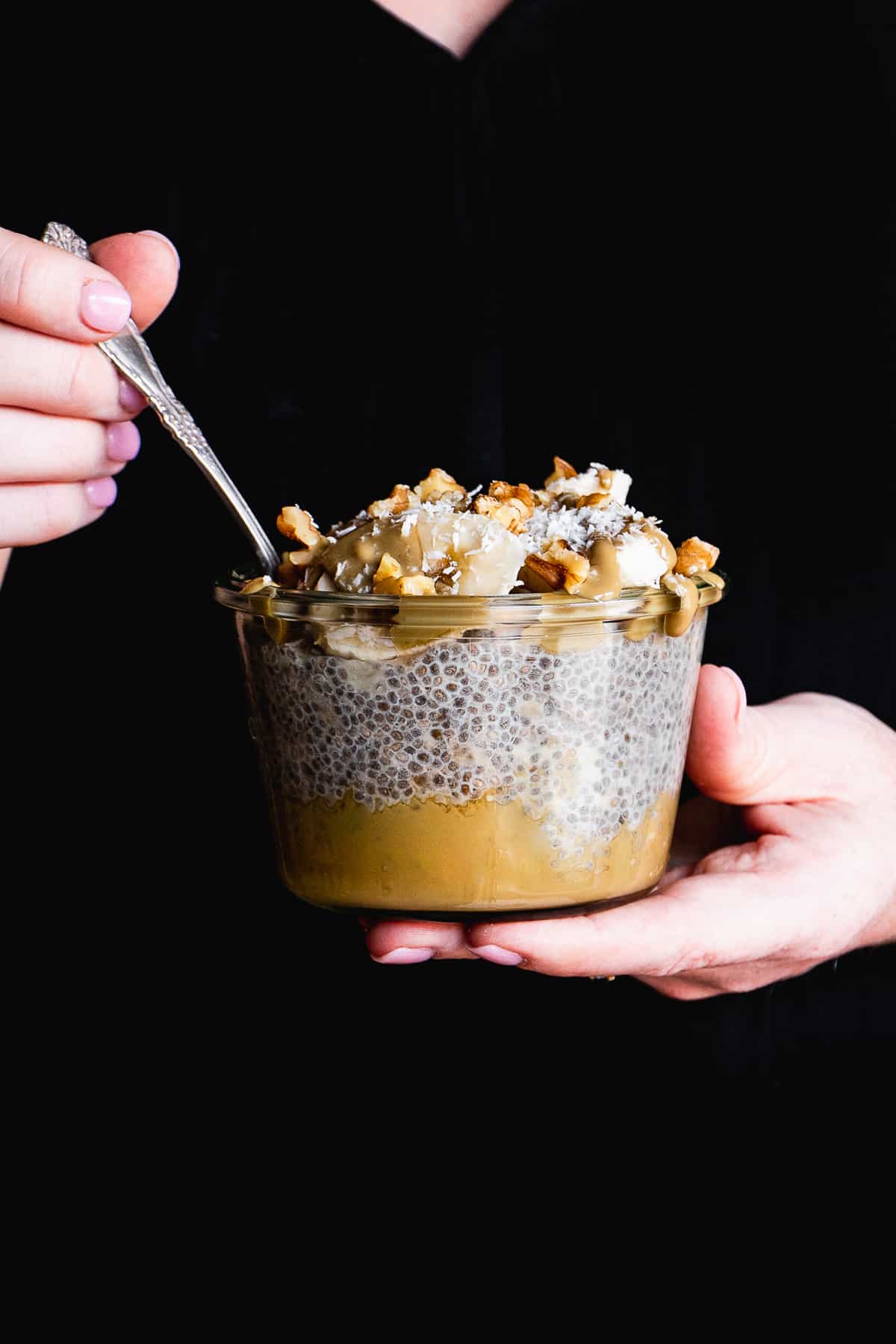 Person holding chia pudding in a jar with toppings with a black shirt.