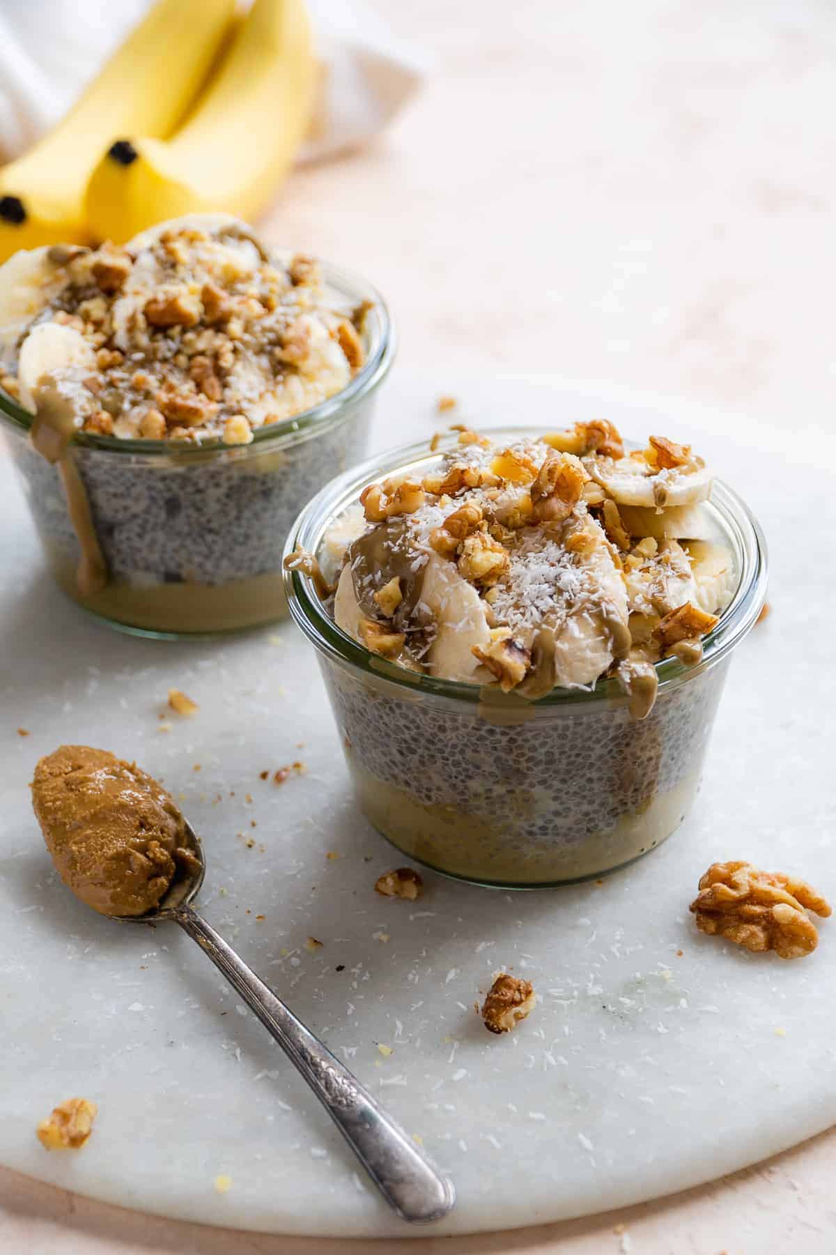 Two jars of chia pudding with toppings on a marble platter.