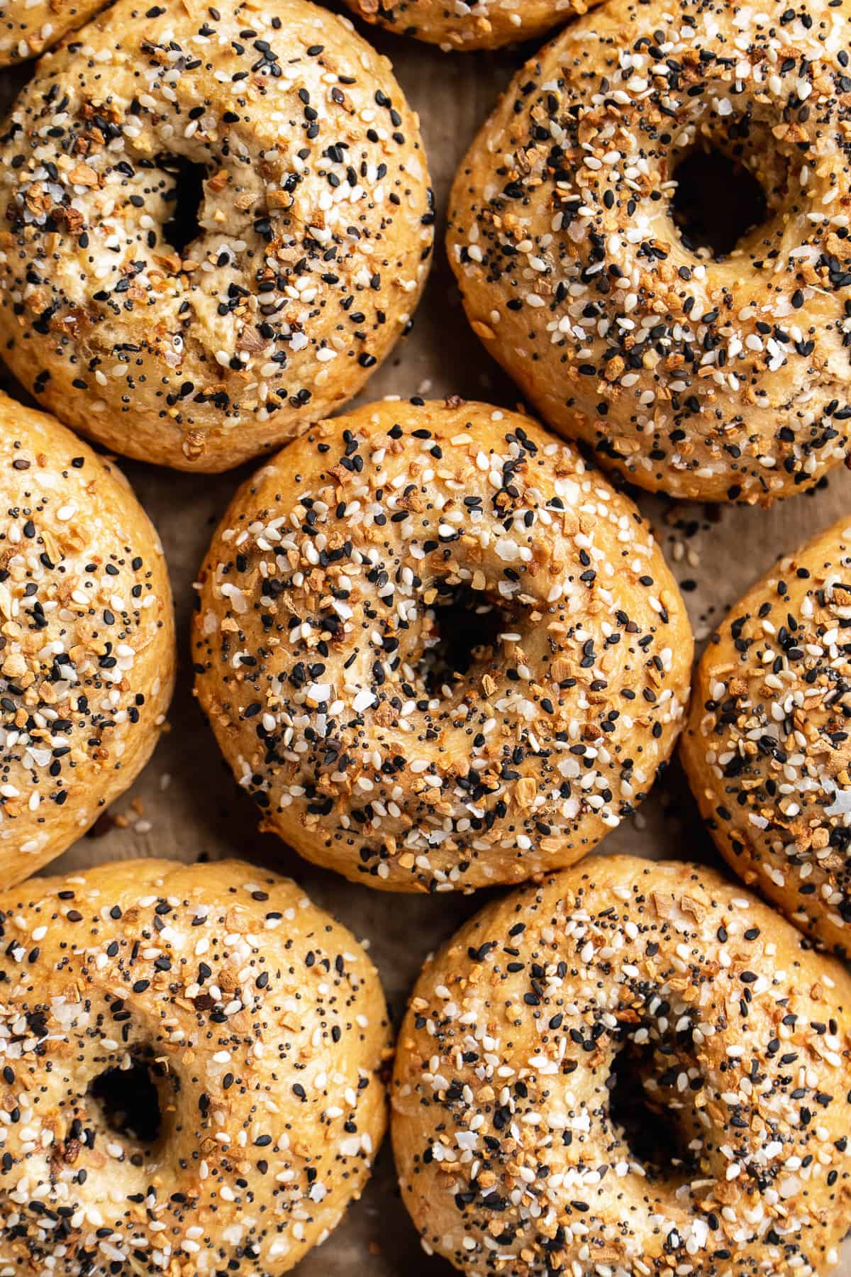 Overhead view of gluten free everything bagels lined up on a baking sheet.