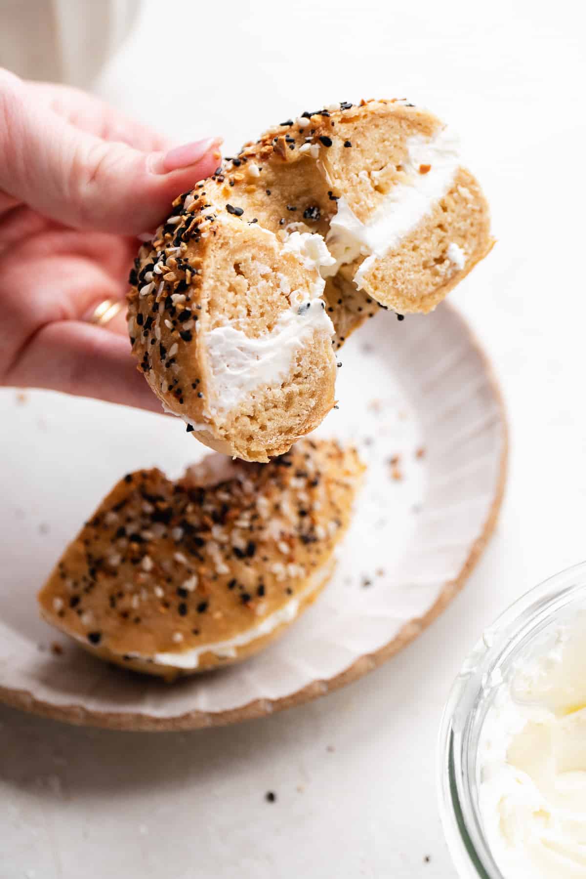 Hand holding a gluten free everything bagel with cream cheese in the middle.