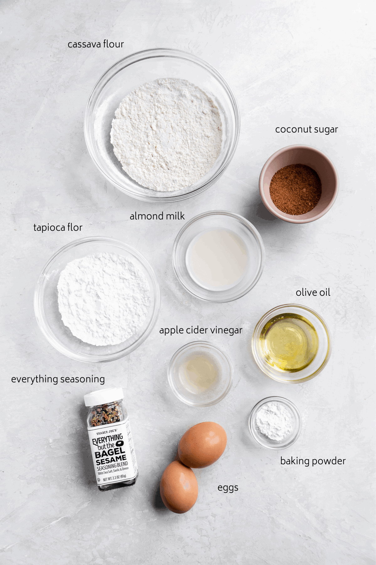 Ingredients for gluten free bagel recipe on a white surface with labels in black.