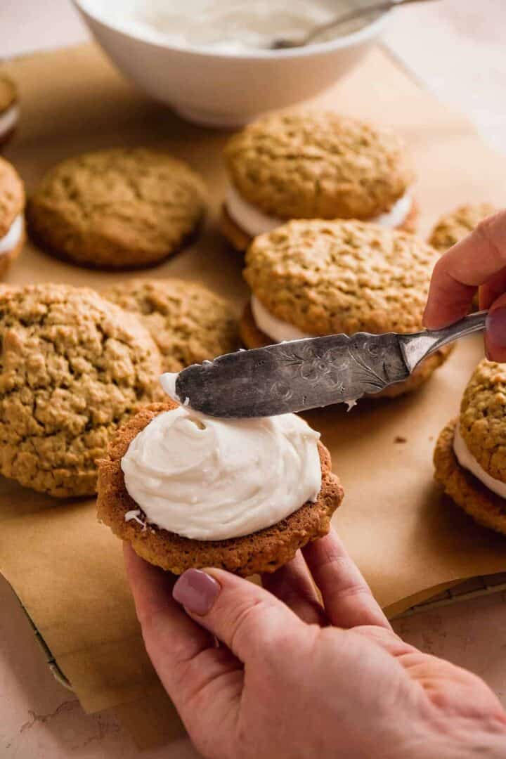 Hand spreading filling over an oatmeal cookie.