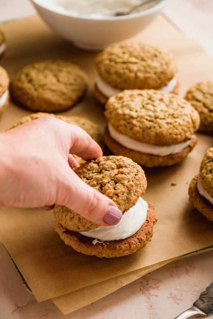 Person sandwiching two gluten free oatmeal cookies with filling in the middle.