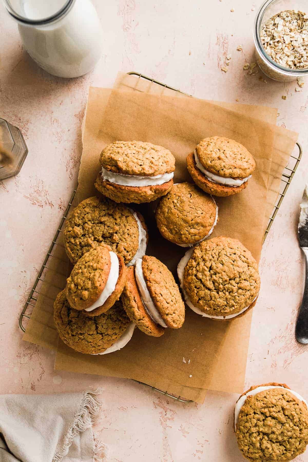 A wire cookie rack with brown parchment paper and gluten free oatmeal cream pies scattered on top.