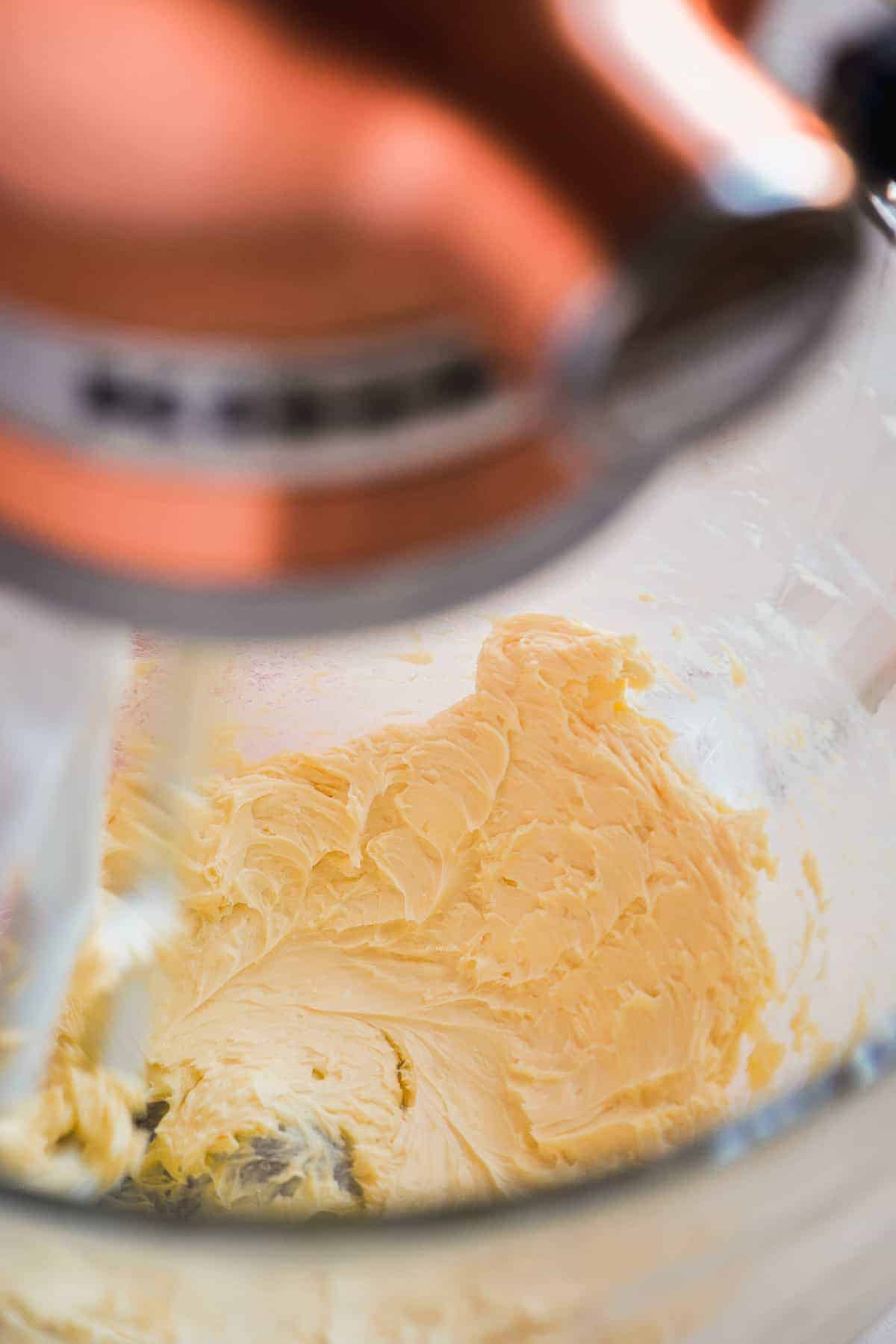 Mixer beating butter in a glass bowl.