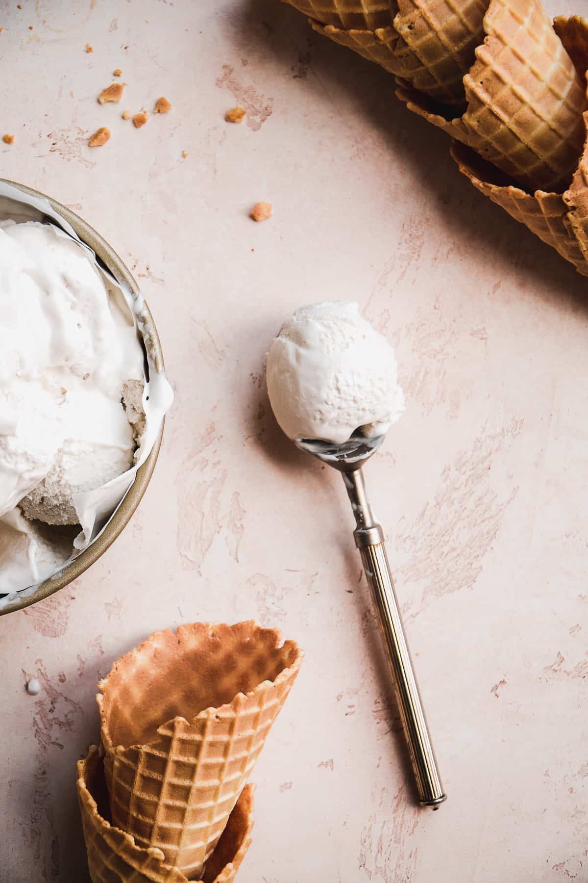 Ice cream scoop with dairy free vanilla ice cram on a pink surface.