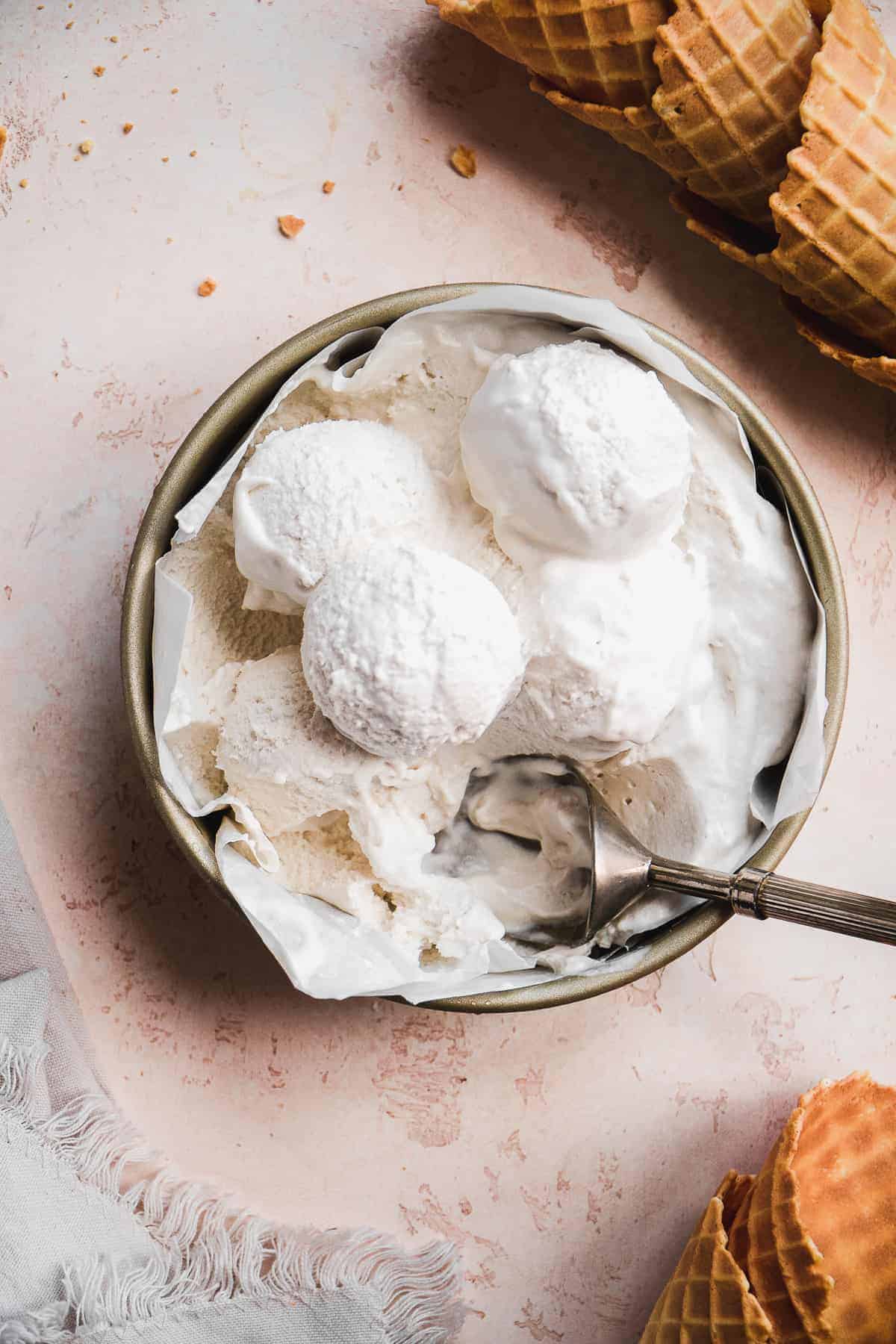 Overhead view of coconut milk ice cream in a container with an ice cream scoop inside.