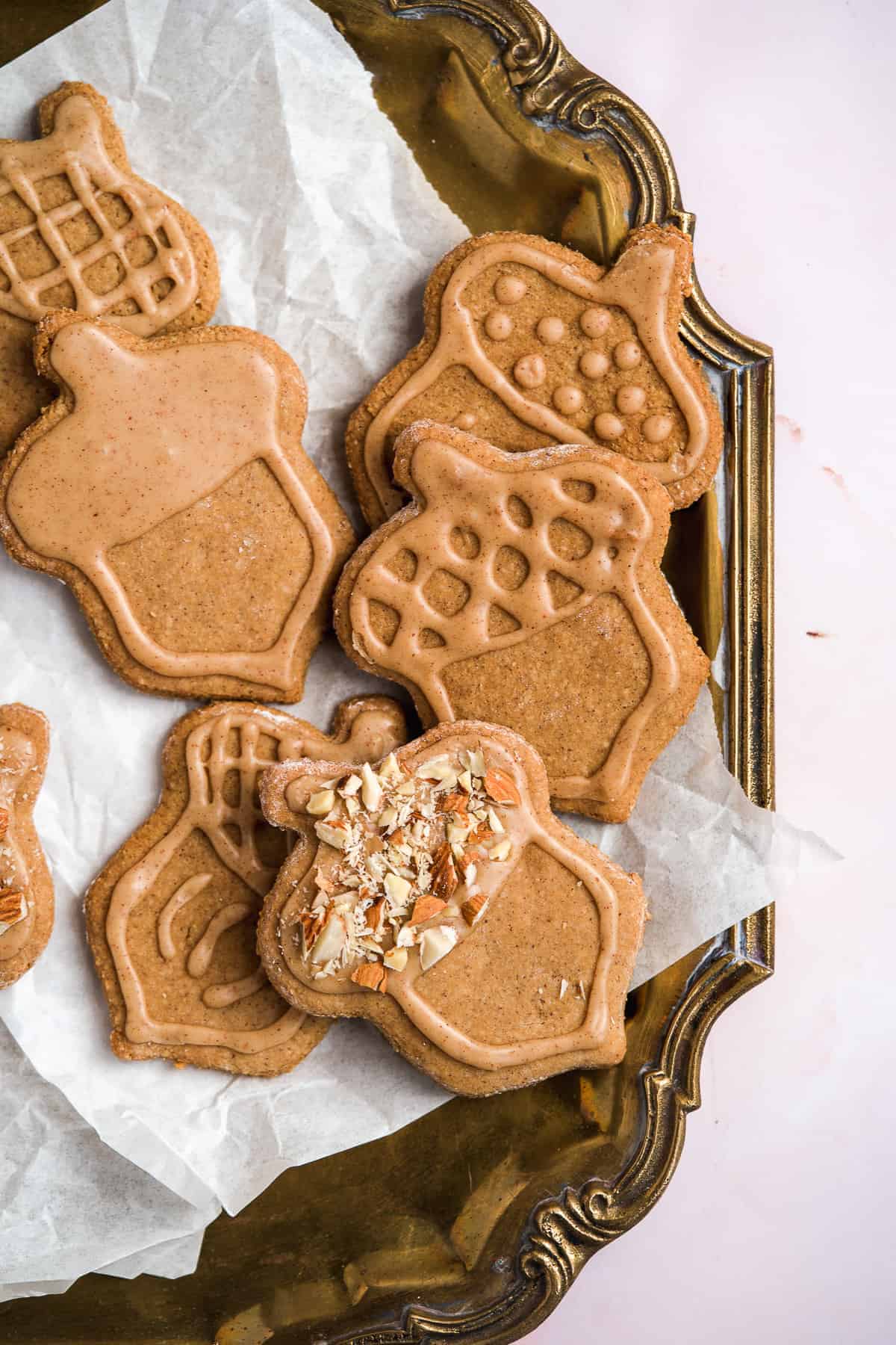 Close up overhead photo of freshly baked and decorated acorn shaped almond flour peanut butter cookies on parchment paper on a gold tray.