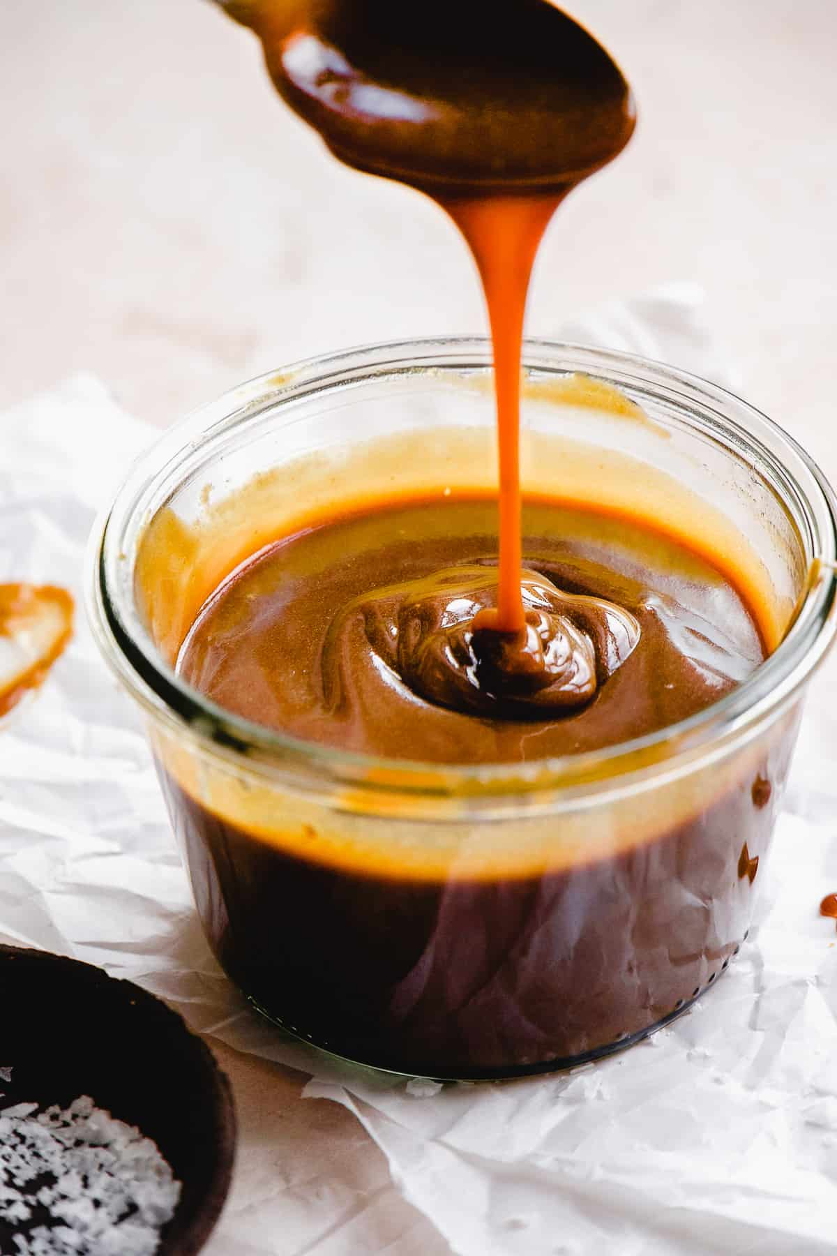 Dairy free caramel dripping off a spoon and running into a glass container.