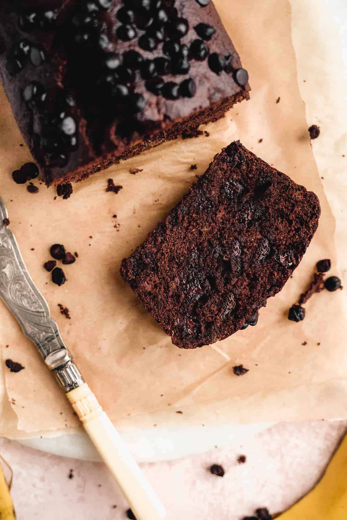 Healthy double chocolate banana bread loaf with a slice on a piece of parchment paper and a knife on the side.