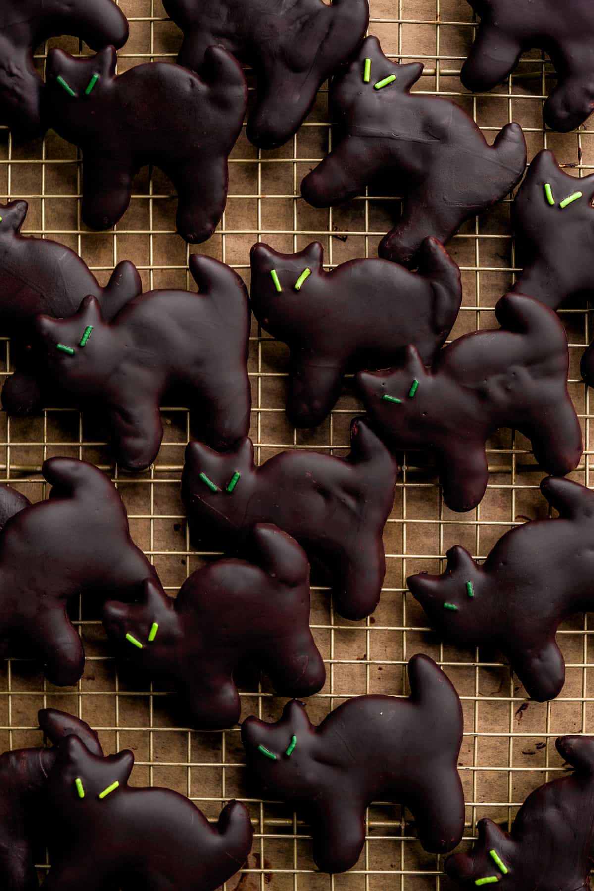 Chocolate black cat cookies with green eyes on a wire rack.