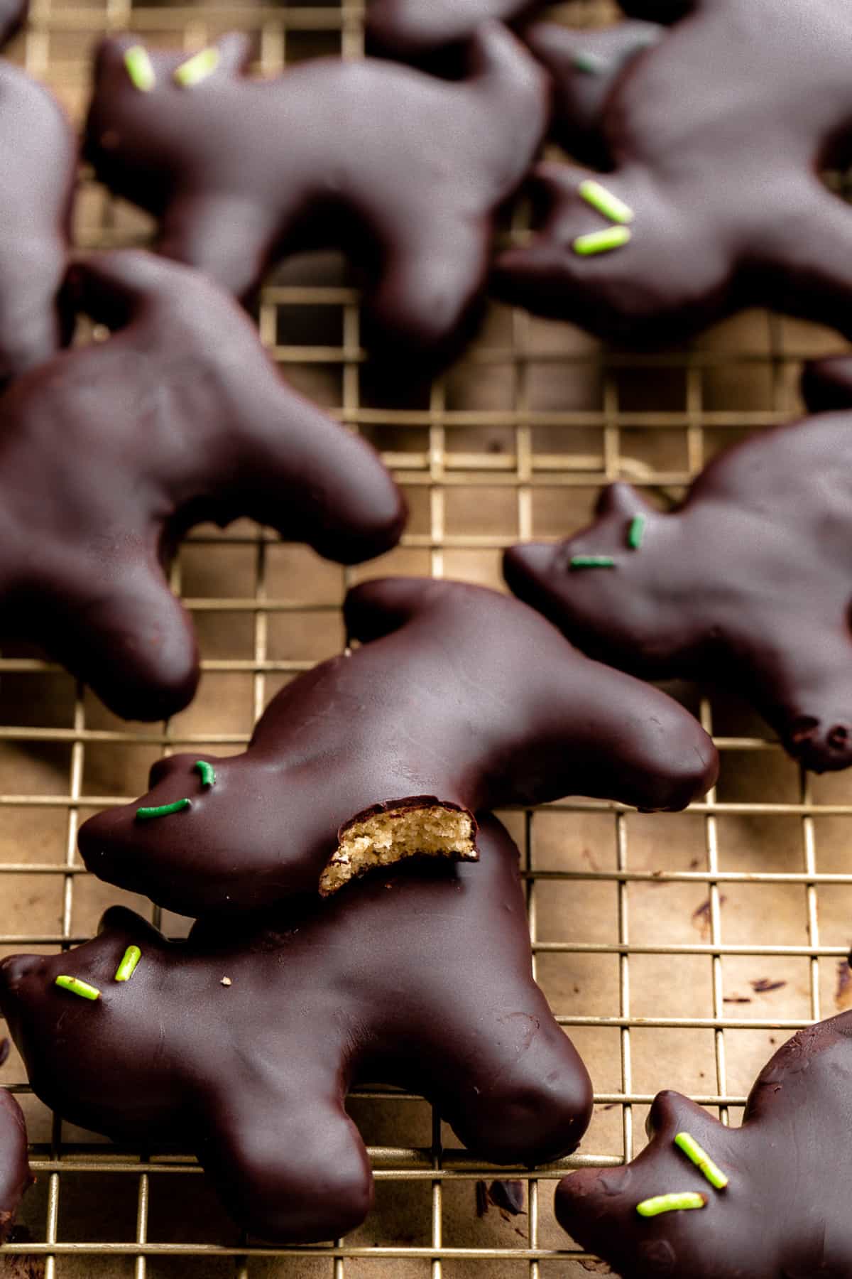 Chocolate coated black cat cookies with green eyes and a bite taken out of one scattered on wire rack.