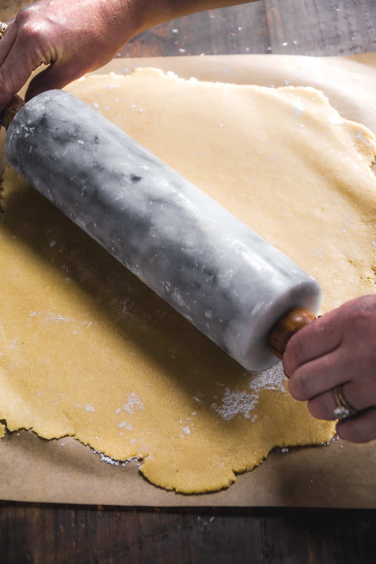 Person rolling out gluten free sugar cookie dough on parchment paper with a rolling pin.