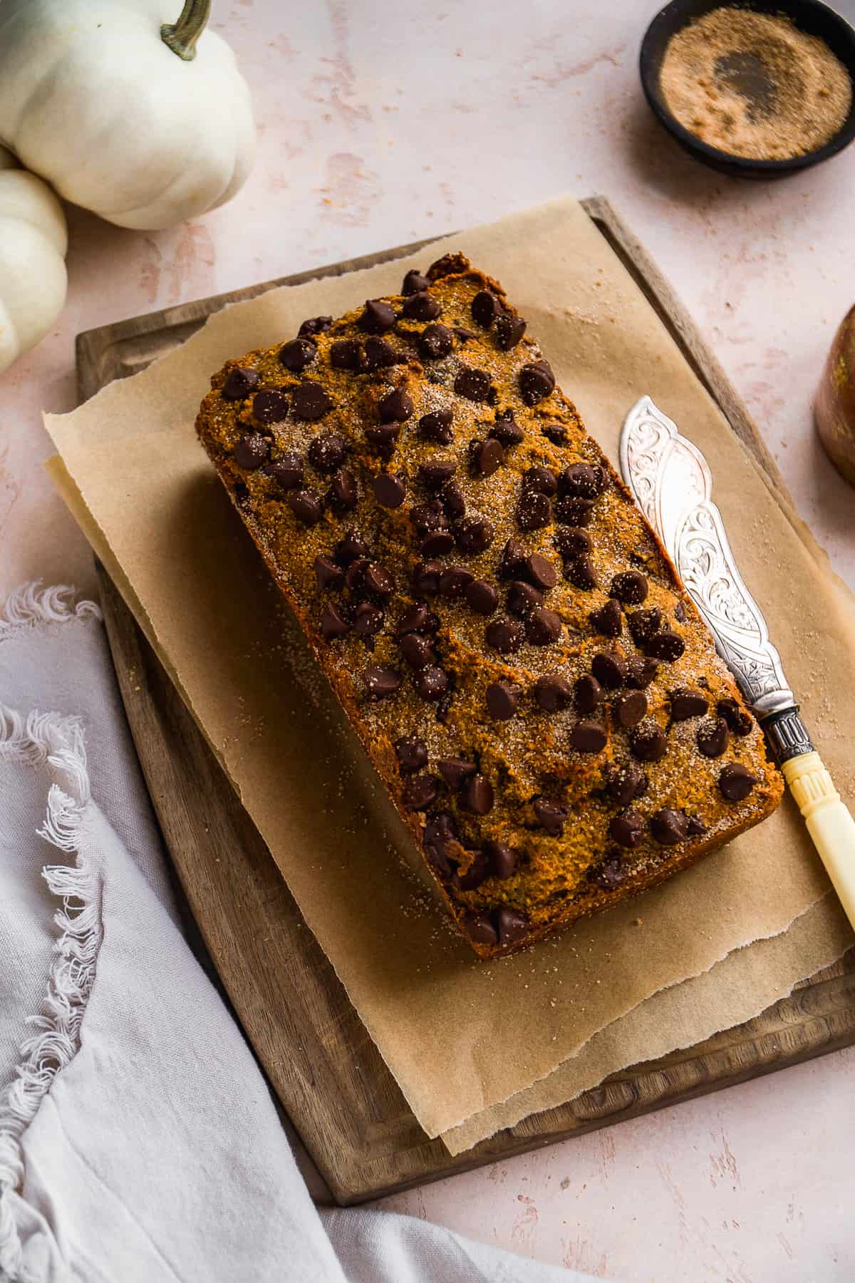 Pumpkin bread with chocolate chips on top on a wooden cutting board with a knife on the side.