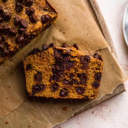 A slice of chocolate chip pumpkin bread laying face up on a wooden cutting board.