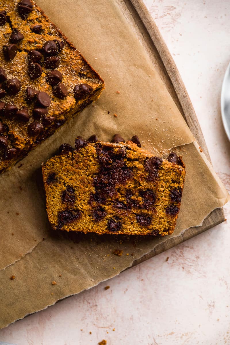 A slice of chocolate chip pumpkin bread on a wooden cutting board facing up.