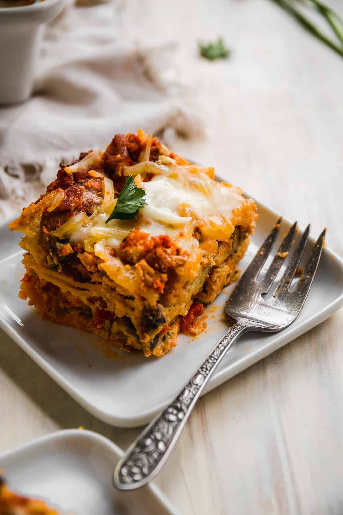 Slice of gluten free lasagna on a square plate with a fork.