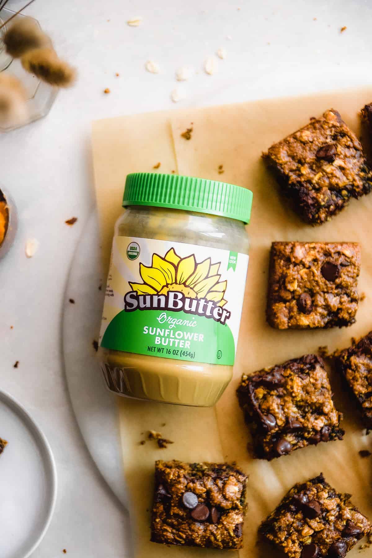 Pumpkin bars on a piece of parchment paper with a jar of sunflower butter with a green label is resting to the side.