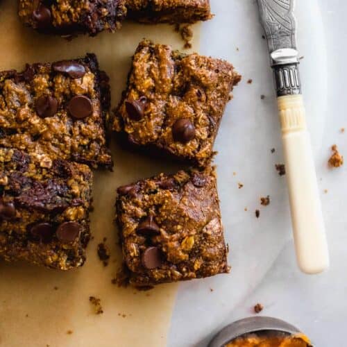 Gluten free pumpkin bars scattered on parchment paper with a measuring cup filled with pumpkin off to the side.