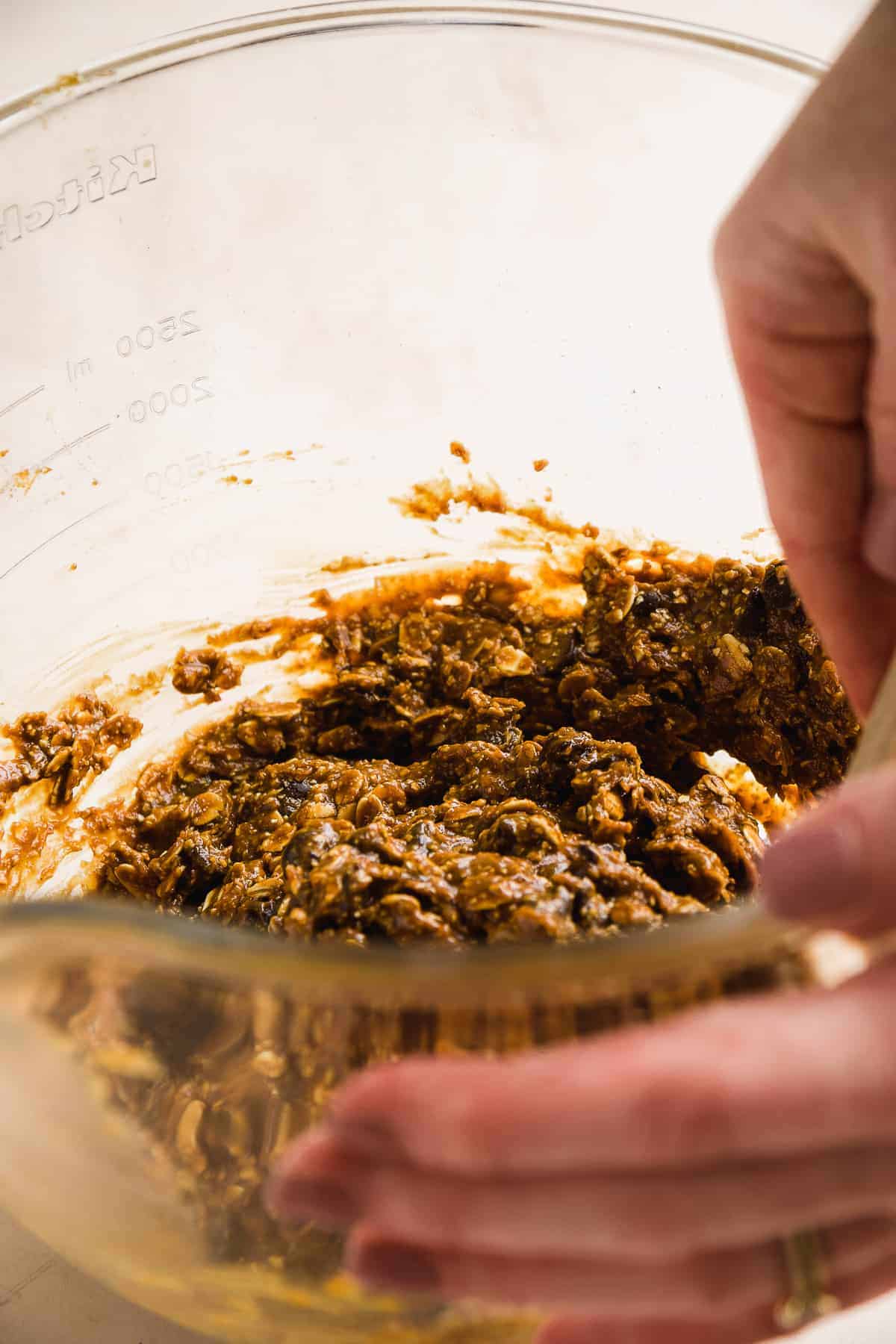 A glass bowl with someone folding chocolate chips into the oatmeal cookie dough.