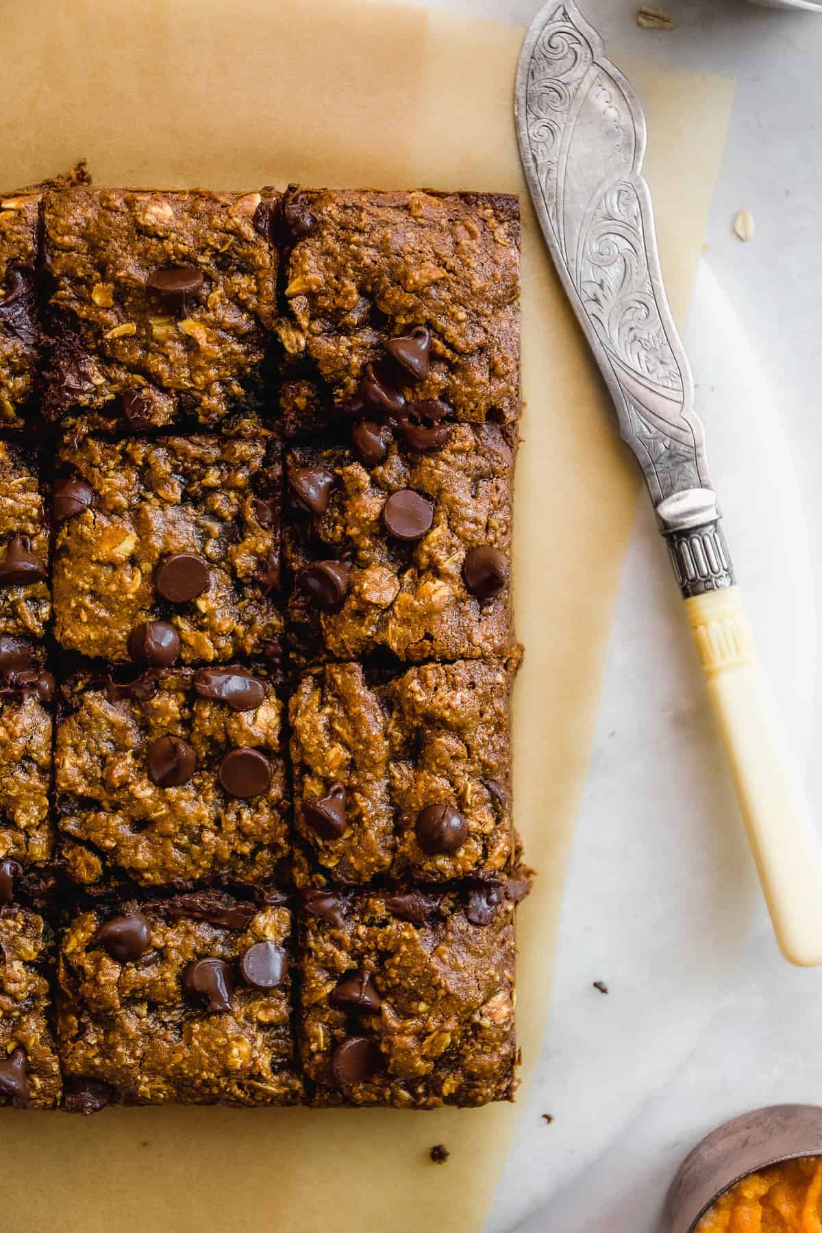 Gluten free pumpkin bars on a marble platter sliced into squares with a knife off to the side.